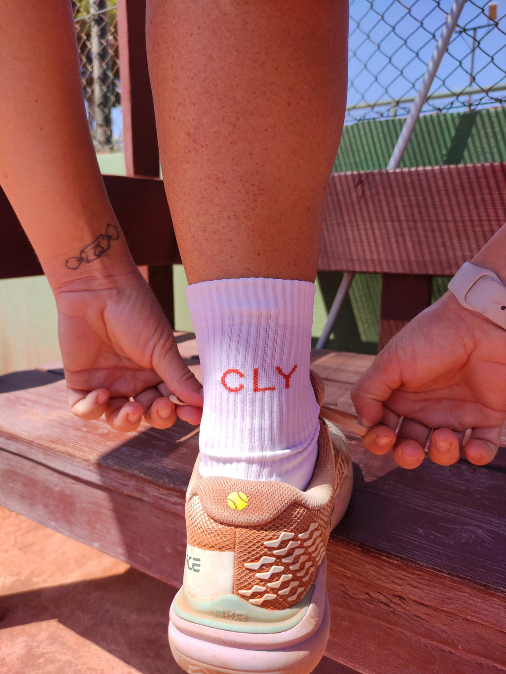 Jugadora de tenis atándose la zapatilla con calcetines CLY ZERO en la pista